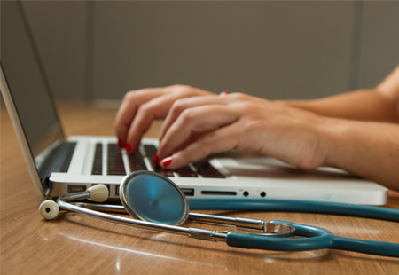 Bild: Person arbeitet am Laptop, daneben liegt ein Stethoskop | National Cancer Institute, unsplash.com